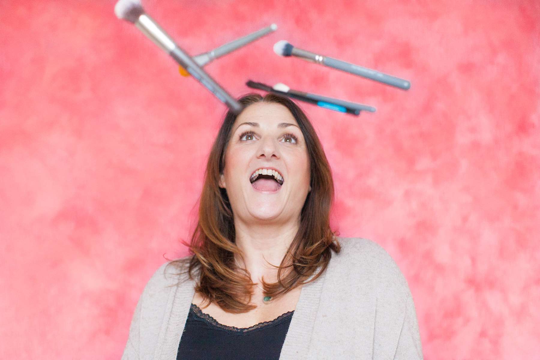smiling make up artist throwing brushes up in the air at a headshot brand session