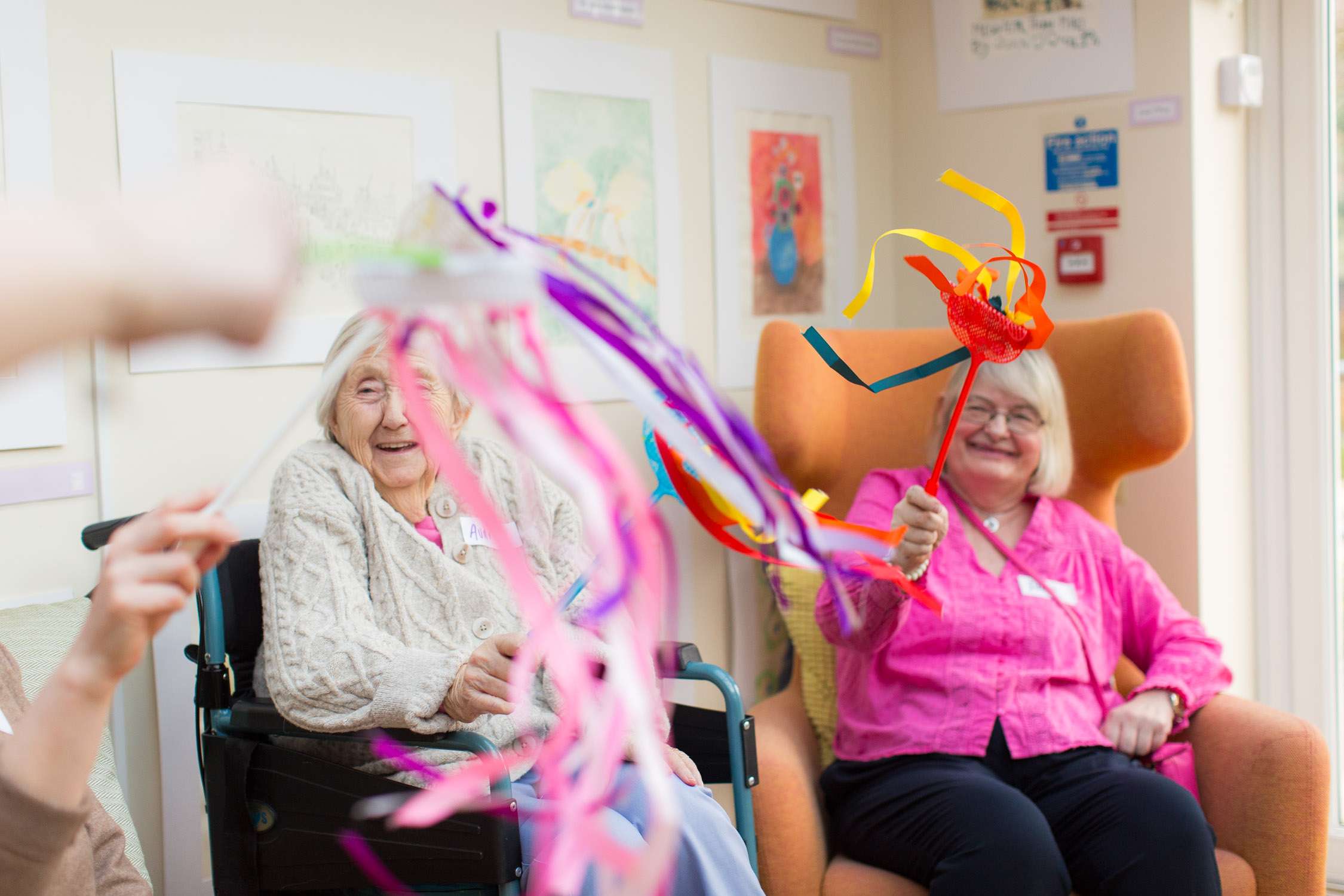 two care home residents look on joyfully while playing with ribbons flying in air