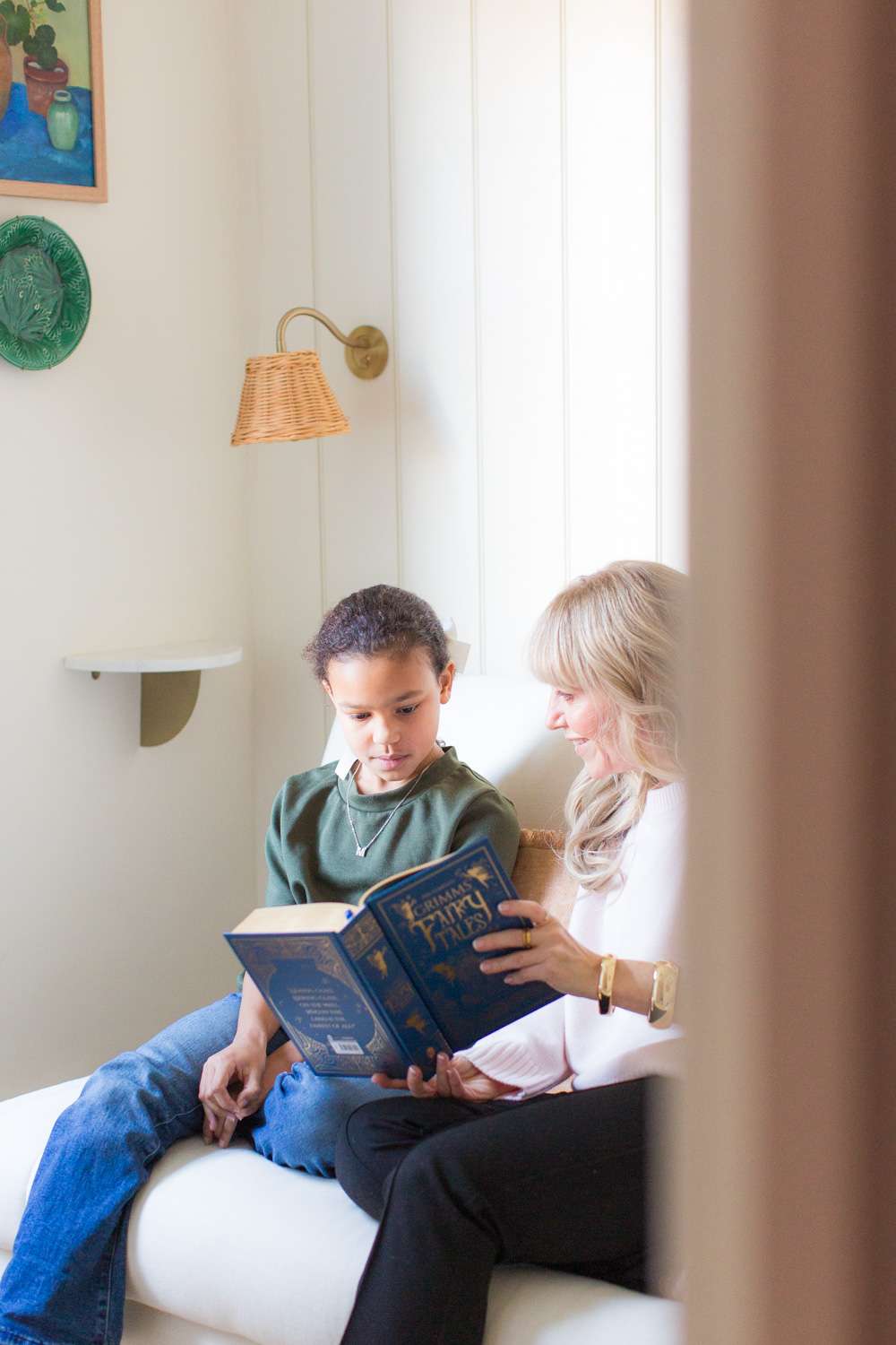 peeking in through doorway at woman reading a book with a child sitting on sofa together