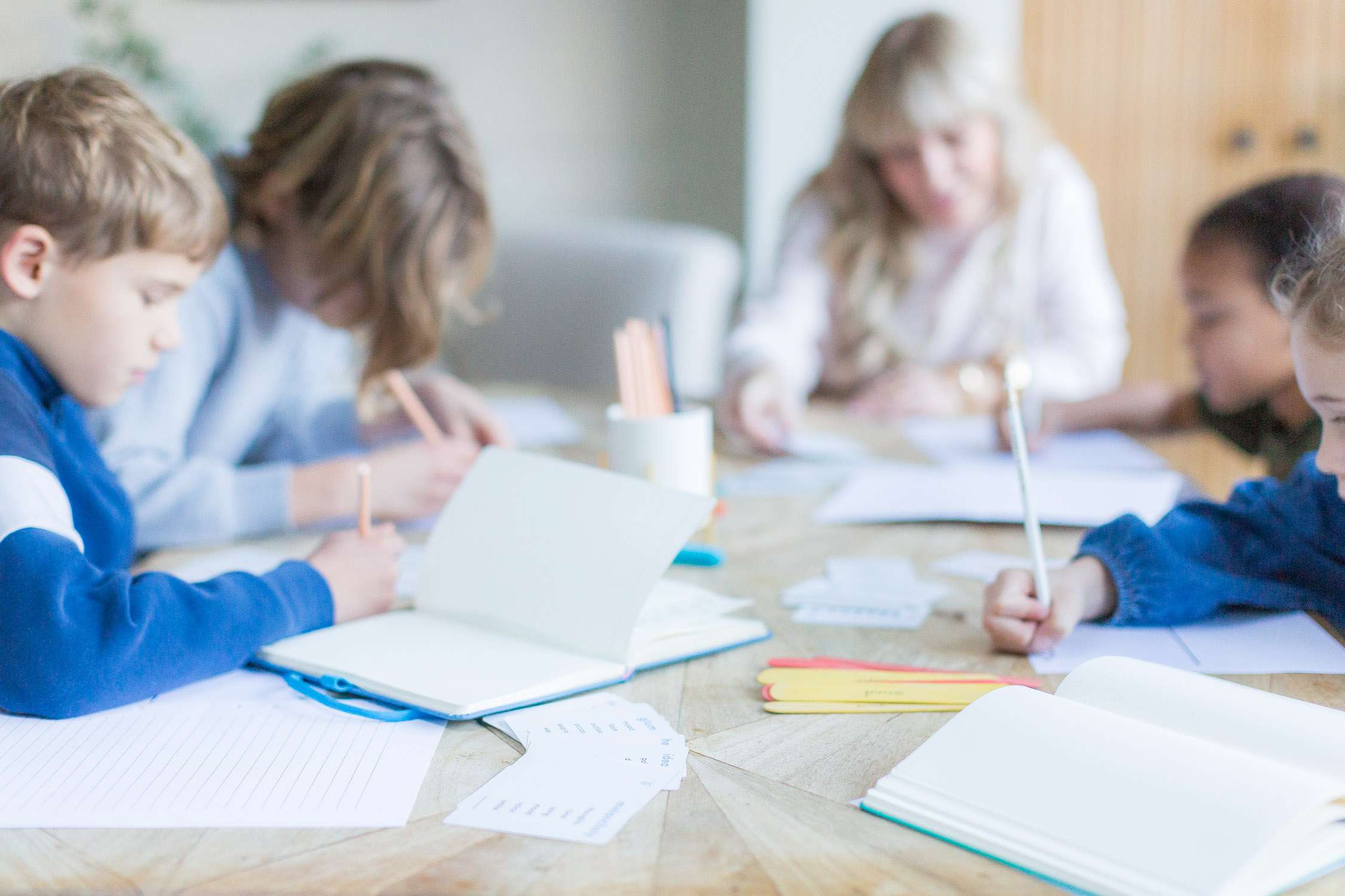 blurred image of a tutor led children's workshop at a south London kitchen table, lots of workbooks and colourful lolly sticks in focal foreground